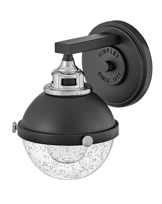 Black and chrome modern wall sconce with an elongated, cylindrical white glass shade, angled view.