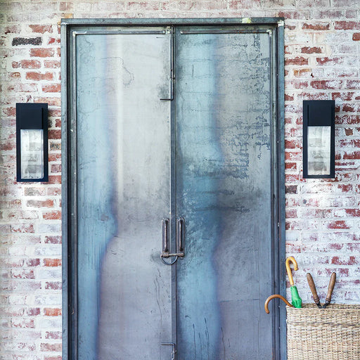 A modern black outdoor wall light with clear glass mounted on a wall.