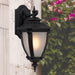 Black outdoor wall sconce with a modern, curved design, illuminated.