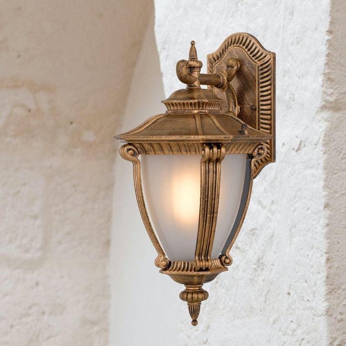 Gold outdoor wall sconce with a modern, curved design, illuminated.