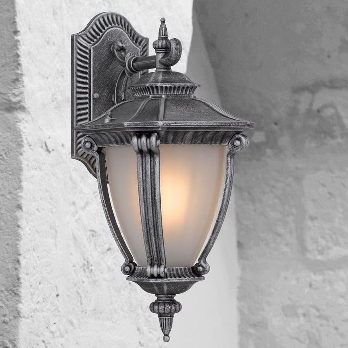 Silver outdoor wall sconce with a modern, curved design, illuminated.