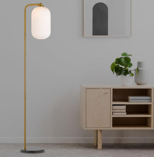 Aged gold floor lamp with an opal glass shade, illuminated.