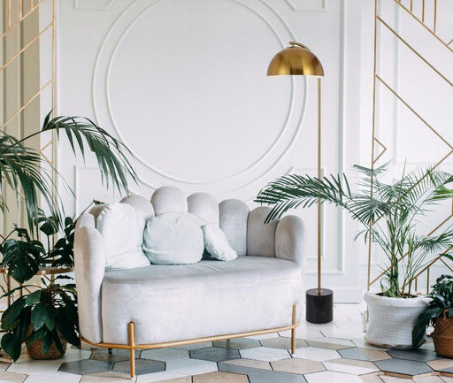 Black and aged gold floor lamp with a spherical glass shade, illuminated.