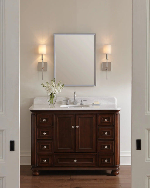 Polished nickel wall sconce with a cylindrical clear glass shade and exposed bulb, in a room setting.