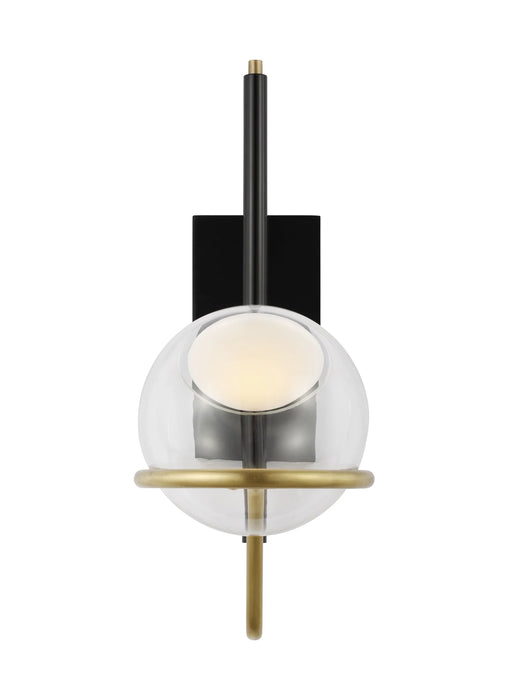 A modern black and brass wall sconce with a cylindrical shade mounted on a light wall.
